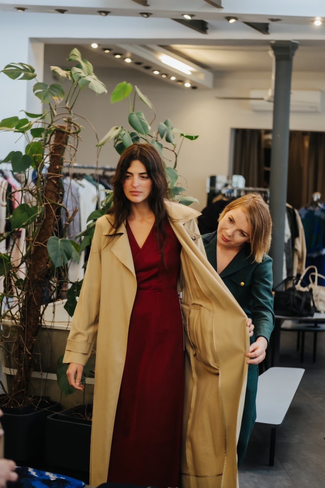 Client trying on a burgundy dress and beige trench in a curated vintage boutique