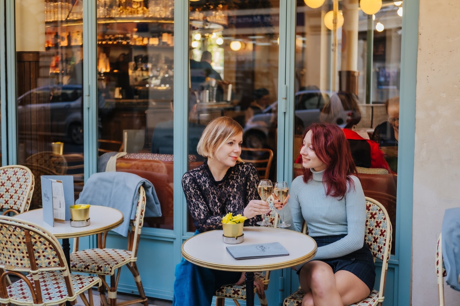Two women clinking sparkling wine glasses at a Parisian café