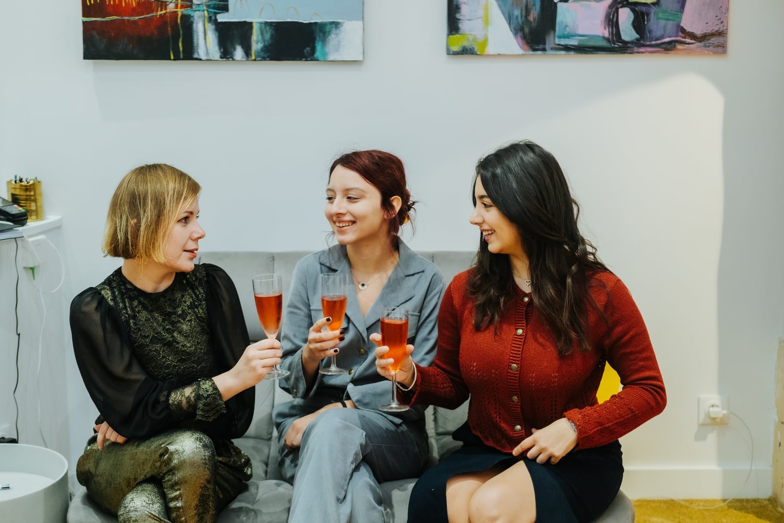 Three clients with cocktails on a velvet sofa in front of contemporary art