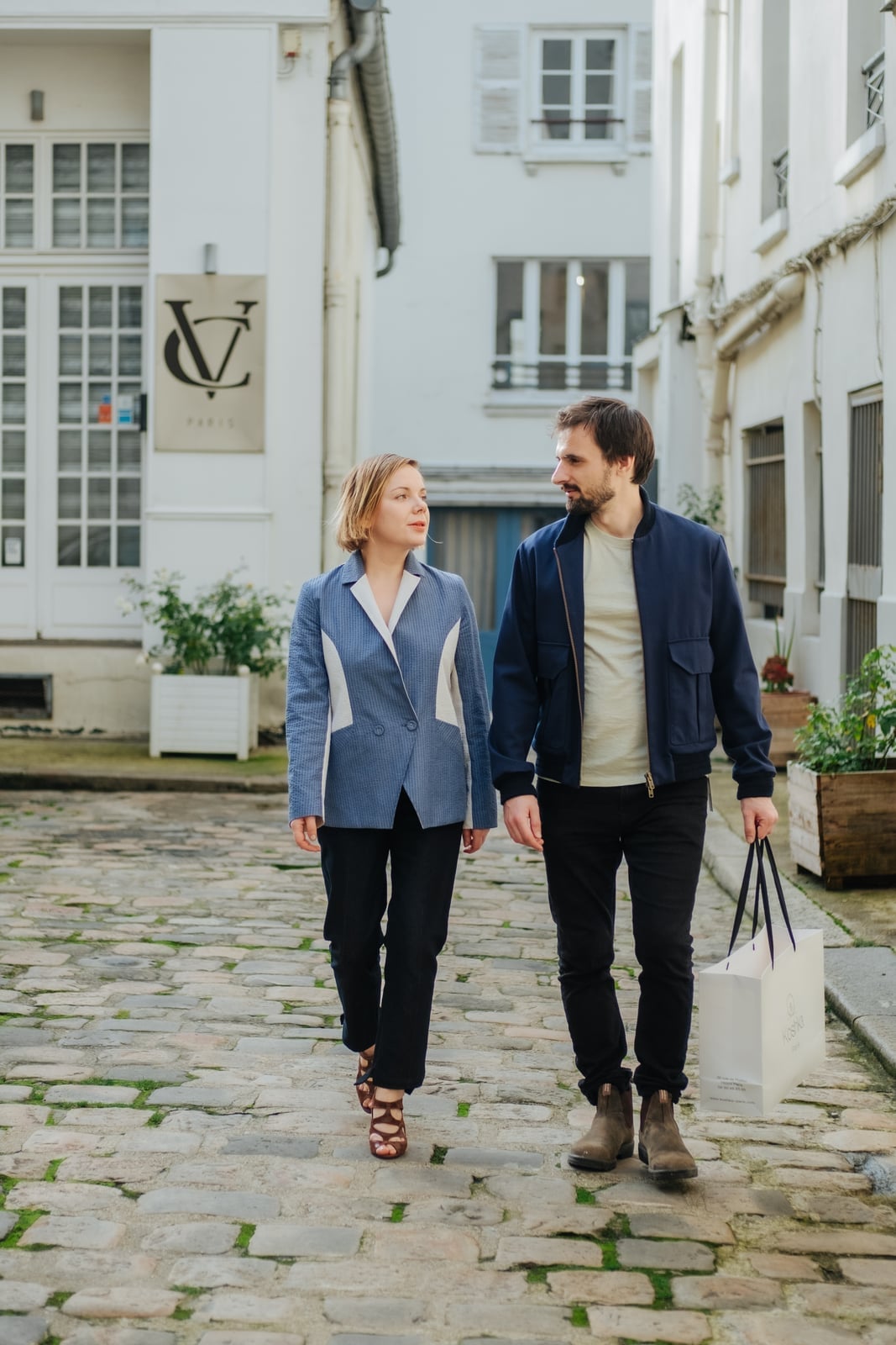 Couple in tailored outerwear walking past a Paris atelier sign