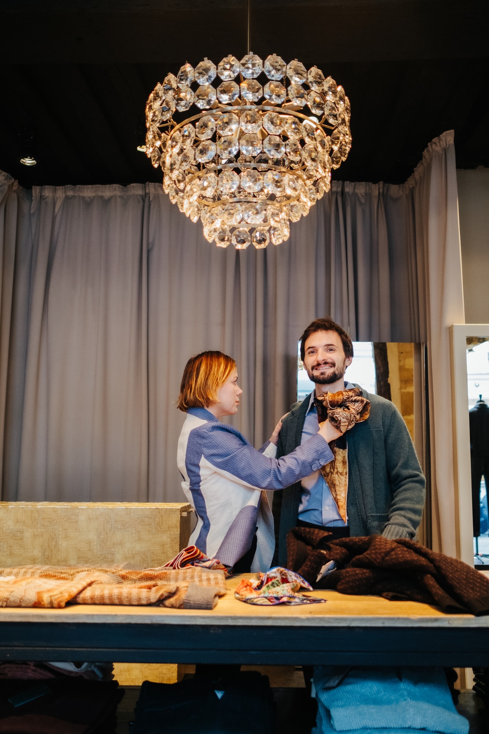 Stylist tying a vintage silk scarf under a crystal chandelier in a Paris vintage boutique